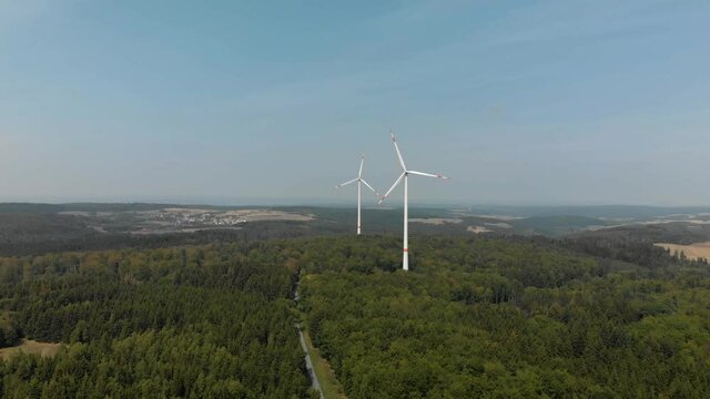 Wide aerial shot if a wind farm in the German countryside, turbines spinning on a a bright sunny day.