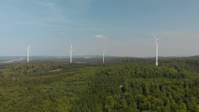 Aerial dolly shot of a cluster of wind turbines in the German countryside, bright blue sky day.