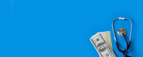 Stethoscope and a bundle of dollar bills on a blue background. Medical banner for website copy space, top view - Powered by Adobe