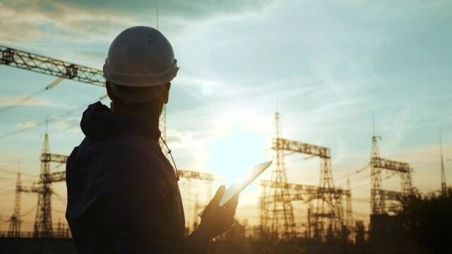 electrical worker silhouette engineer a working with digital tablet, near tower with electricity. energy business technology industry concept. electrical studying reading documents on power tablet
