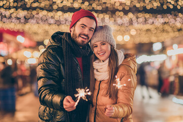 Photo of bonding couple celebrate x-mas christmas lights sparklers under outdoors illumination wear season outerwear
