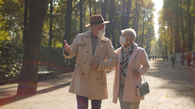 Mature Couple Wearing Sterile Face Masks Walking In Autumn Park