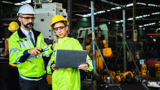 Industrial engineer in suite and safety helmet working in factory, planning and training with laptop with workers