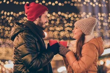 Photo of two people couple toast hot coffee beverage mug under outdoors evening x-mas spirit lights wear season outerwear