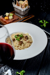 risotto in a white plate on a black background with red wine
