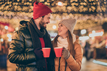 Photo of two people couple clink hot coffee beverage mug under evening x-mas lights wear season outerwear