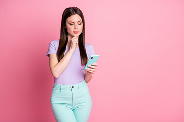 Photo of minded smm girl use smartphone think thoughts decide social network post wear teal pants violet clothes isolated over pink color background