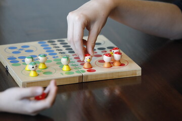 Board game ludo with child's hand, toy figure and red die.