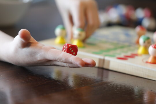 Board game ludo for children with hand, colorful toy figure, red dice.