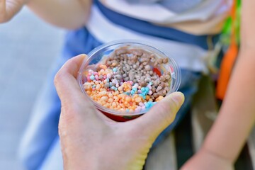 The hand of an adult gives the child a mini ice cream. Small multicolored balls.