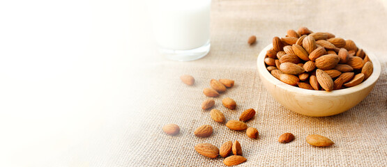 Almond nuts in wooden bowl and blurred almond milk in background on a wooden table. Wider banner with copy space. High quality photo