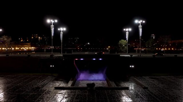 Ekaterinburg city center with Iset River and plotinka. Stock footage. Aerial view of night cityscape with the dam of the city pond on the Iset River with falling purple water illuminated by neon