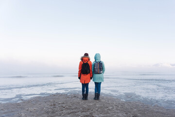 two girls in bright winter jackets do not admire the sweeping sea on the snowy shore beyond the Arctic Circle on a frosty winter day