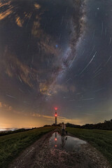 Panorama of the full sky, a man standing on the road looks at the reflection in the water under a...