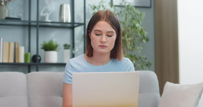 Creative young woman teleworking while sitting on sofa in living room. Attractive brooding Caucasian female student studying and thinking of project at home. E-learning, technology concept.