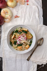 Top View of White Bowl with Vegan Ramen Soup Against a Black Background with Red and White Raw Cipollini Onions in the Background