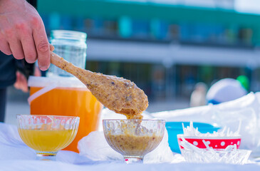 A man's hand holds a wooden spoon, with the help of which bee honey is placed in a glass vase