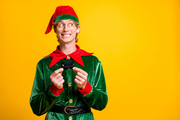 Photo of guy hold debit card look side empty space wear elf velvet green costume cap specs isolated yellow color background