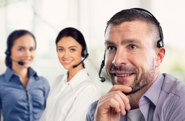 A smiling young businessman call center agent wears a wireless headset at the workplace.