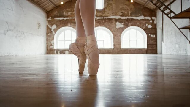 Legs of unknown ballerina in white nylon tights and pointe shoes spinning while dancing at a spacious loft