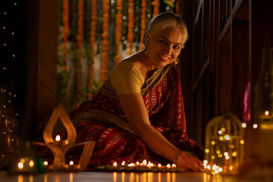 A SENIOR ADULT WOMAN HAPPILY PLACING DIYAS ON FLOOR WHILE SMILING AT CAMERA	