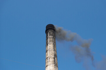 古い煙突から立ち上る黒い煙と青空