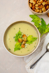 Top View of Bowl of Creamy Celery Soup with Croutons, Celery Leaves, and Dill with a Bowl of Croutons on a Light Tan Background