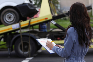 Woman insurance agent prepares documents for car that is taken away by tow truck. Voluntary car insurance concept.