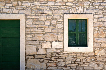 Traditional Mediterraneann house with stone facade and green wooden window and door, in Vela Luka, Croatia.