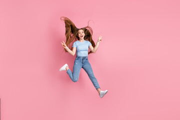Photo portrait of screaming girl showing two v-signs jumping up isolated on pastel pink colored background