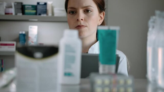 The girl pharmacist conducts an audit of medical products in the pharmacy. Caucasian woman with an electronic tablet checks the presence of drugs creams and tablets on the shelf in the pharmacy.