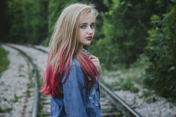 Naklejka premium Young girl on the railroad in the forest. She is dressed in summer style, she has long white and pink hair and blue eyes.