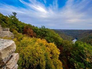 Fototapeta na wymiar View from the top of Cooper’s Rock in Coopers Rock State Forest in West Virginia right before sunset with the valley of fall colored trees below, the water running through and a beautiful blue sky
