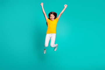 Fototapeta na wymiar Full length photo of ecstatic girl jump raise fists wear yellow t-shirt white pants trousers isolated on turquoise color background