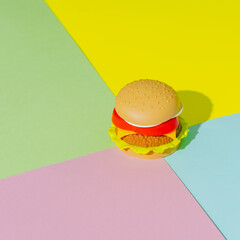 Appetizing burger with shadow on green, yellow and pink background. Creative concept. Plastic pop...