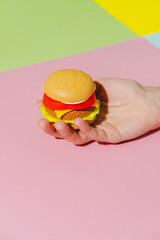 Burger in hand on yellow, green and pink background. Creative concept. Plastic pop art isometric style. Minimalism