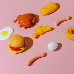 Party meal ingredients like burger, chicken or turkey, sausages, fried egg and croissant on pink background. Creative plastic isometric concept.