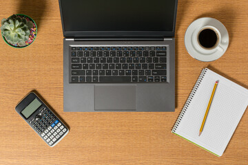 Top view of a workspace with a laptop a notepad with a pencil and a cup of coffee.