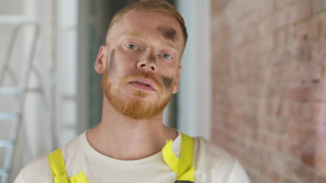 Close up portrait of tired construction worker with dirty stain on face looking at camera