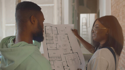 Back view of african couple discussing blueprint of renovating house