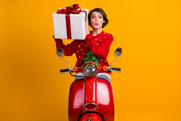 Fototapeta premium Photo of astonished girl in christmas tree ornament sweater pullover shake gift box drive red scooter x-mas eve noel party isolated over bright shine color background