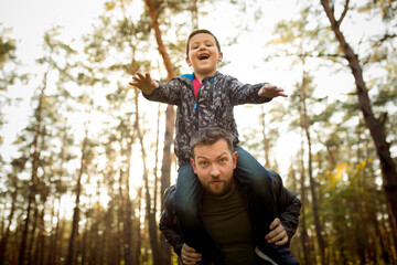 Emotions. Father and son walking and having fun in autumn forest, look happy and sincere. Laughting, playing, having good time together. Concept of family, happiness, holidays, childhood, lifestyle.