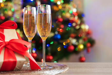 Glass of champagne and gift boxes with large red bow against Christmas tree and defocused bokeh. Soft focus. Copy space. Christmastime celebration concept