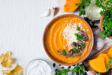Pumpkin soup with croutons, parspey and grated parmesan cheese on light rustic background, dietary vegetarian lunch, top view