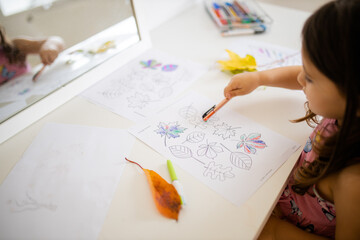 Little girl pointing at a paper sheet with coloring leaves images with a pen