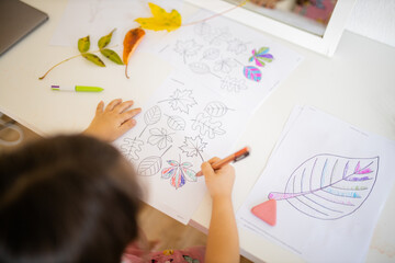 Little girl coloring different types of leaves on a paper sheet with a pen
