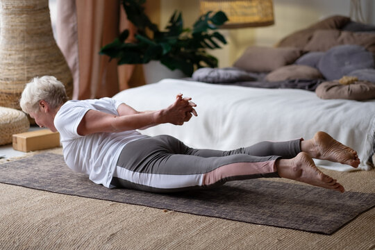 Senior Woman Practicing Yoga At Home Indoor, Doing Salabhasana Or Locust Pose.