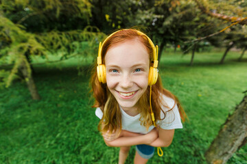 a teenage girl with red hair listens to music with headphones in a Park in the summer.a young woman enjoys and relaxes outdoors on a Sunny day