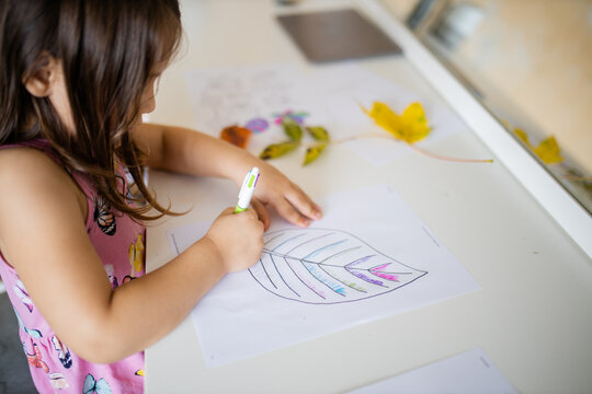Little girl coloring a big leaf image on a paper sheet with a pen