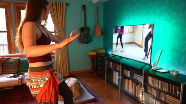 Woman follows workout fitness dance lesson online at home. Exercise watching personal trainer livestreaming on tv social media web channel.